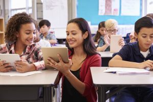 Teacher helping kids with computers in elementary school